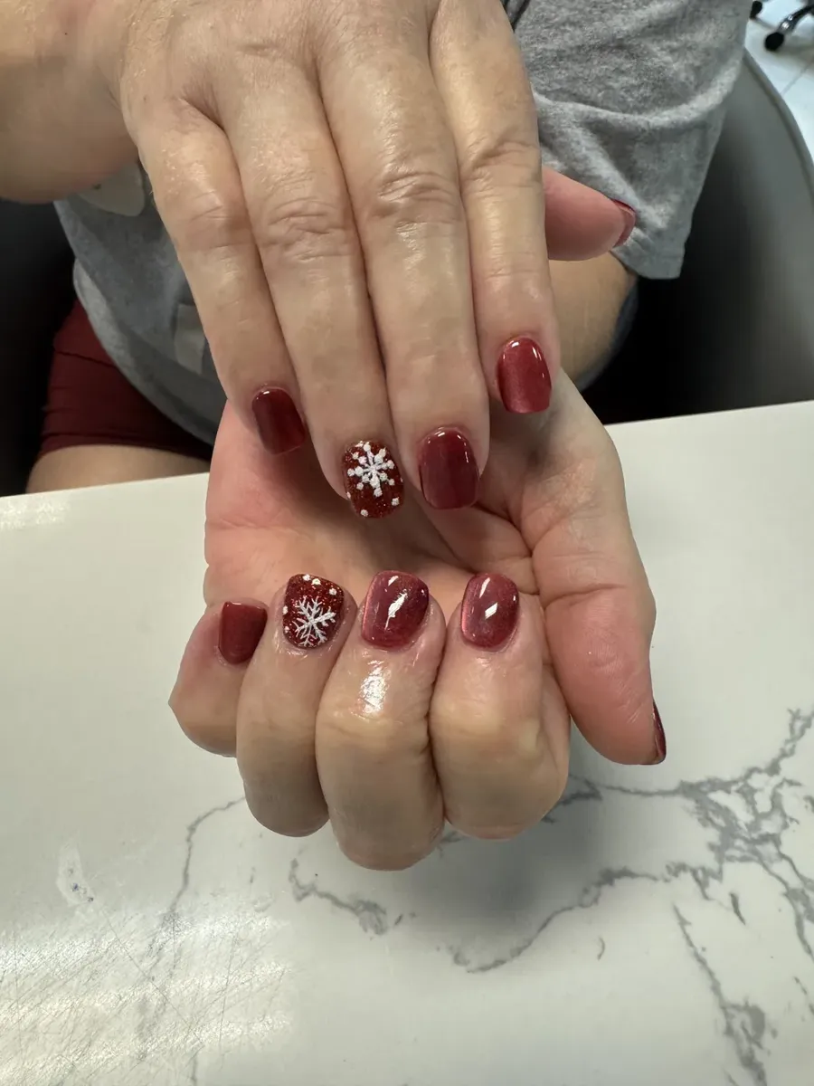 Deep red glossy nails with hand-painted white snowflake art
