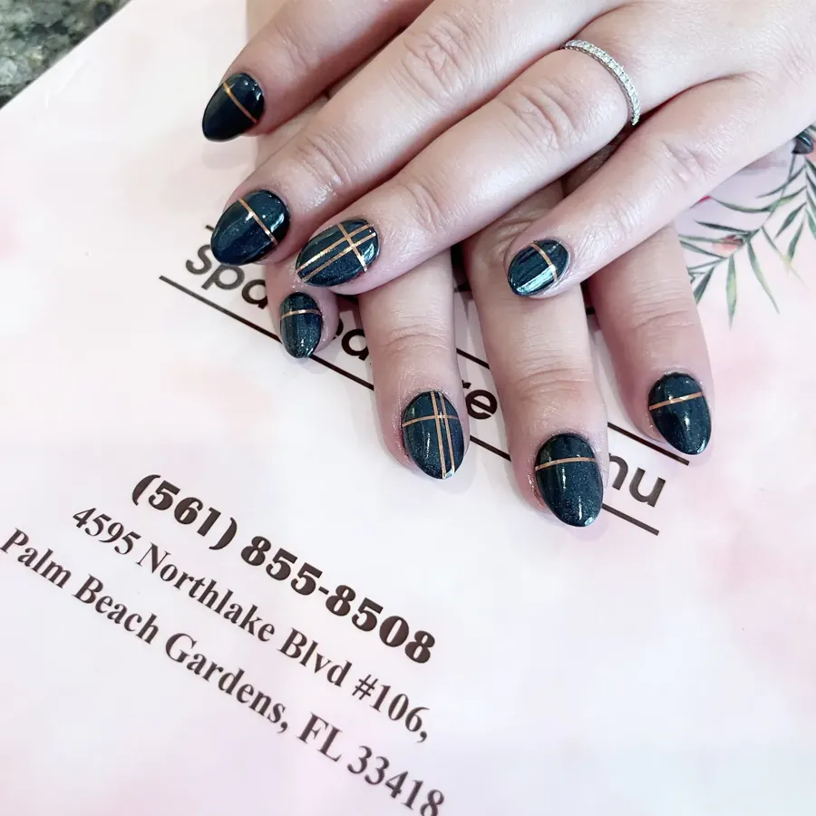 Deep teal nails with fine gold line art, resting on the salon's pink card