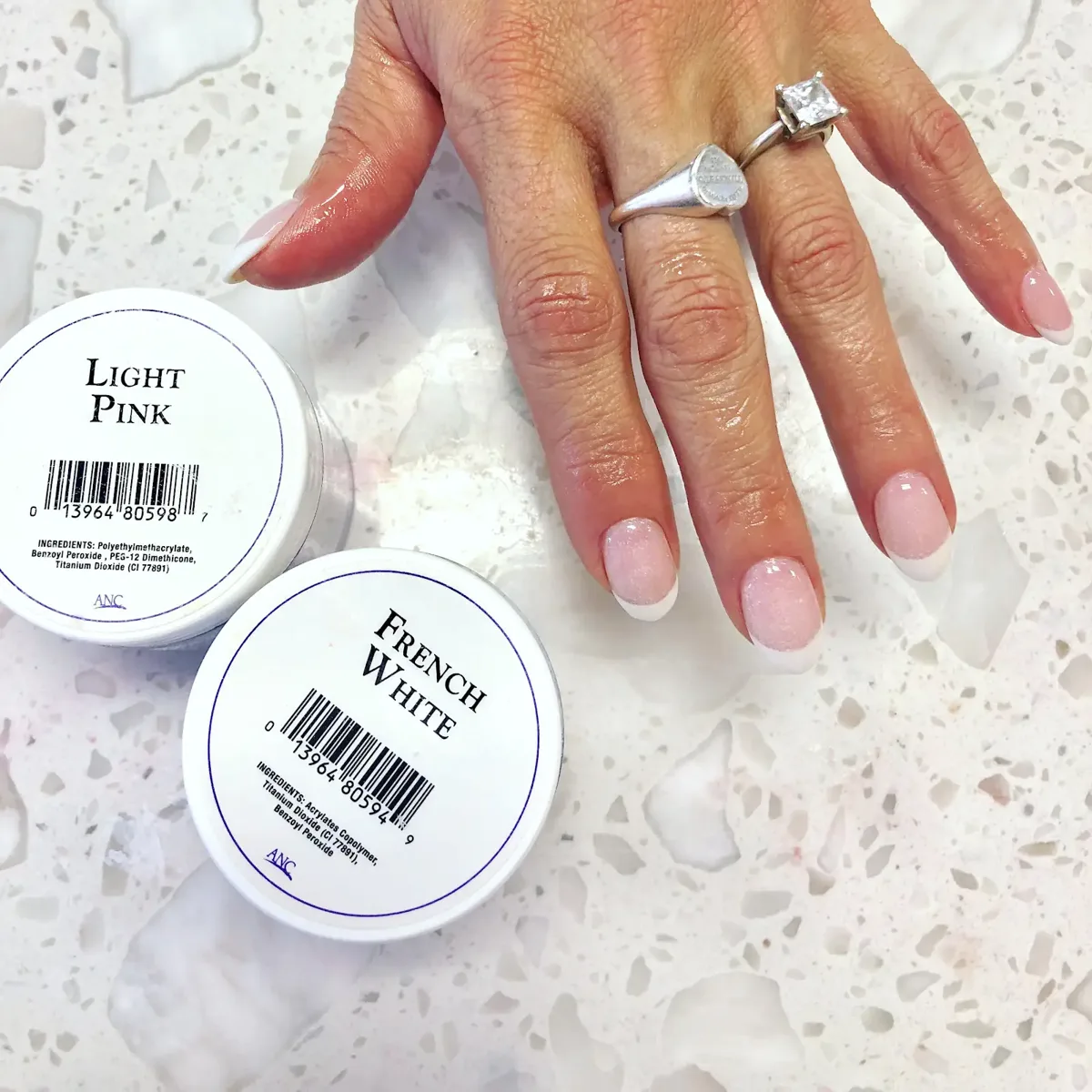Hand with a pink and white French manicure beside jars of light pink and French white dip powder